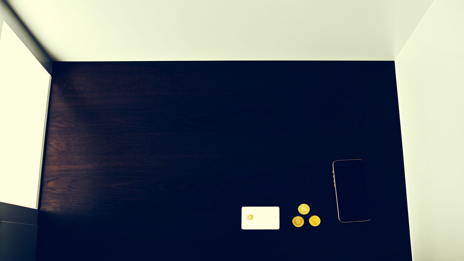 A payment card, a small stack of coins and a phone laid face down on a desk, representing the choice of payment method before a deposit.